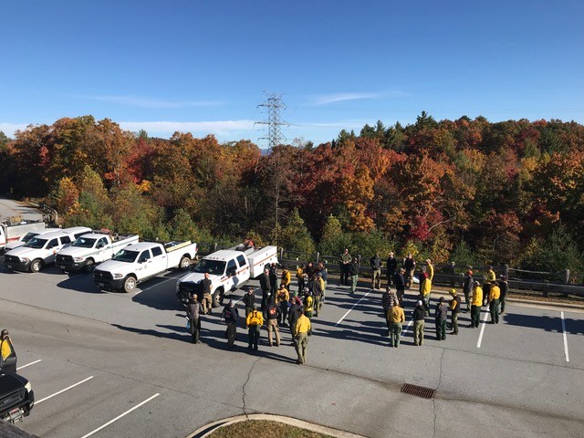 Wildland firefighters gather in a parking lot to brief about a prescribed fire operation. 