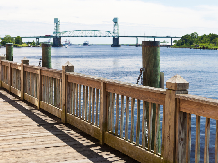Boardwalk along river in Wilmington, NC with a bridge in the background