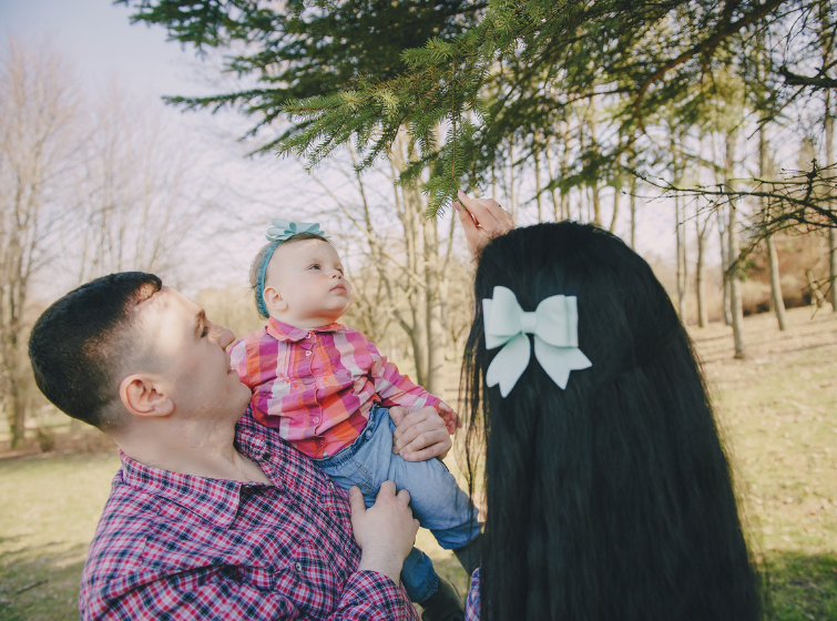 father, mother and baby girl look at the needles of a cypress tree closeup