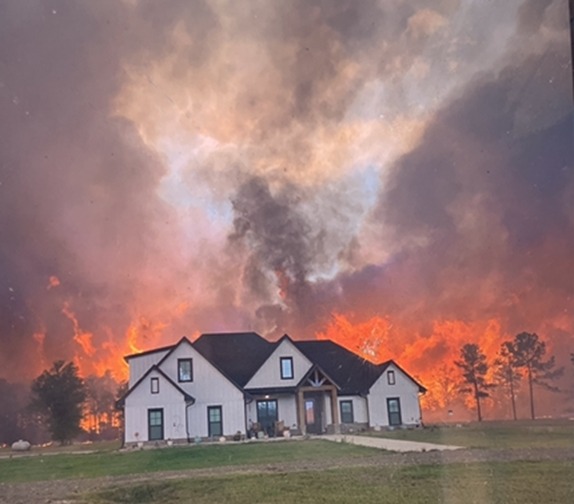 White Louisiana home with intense wildfire flames behind it.