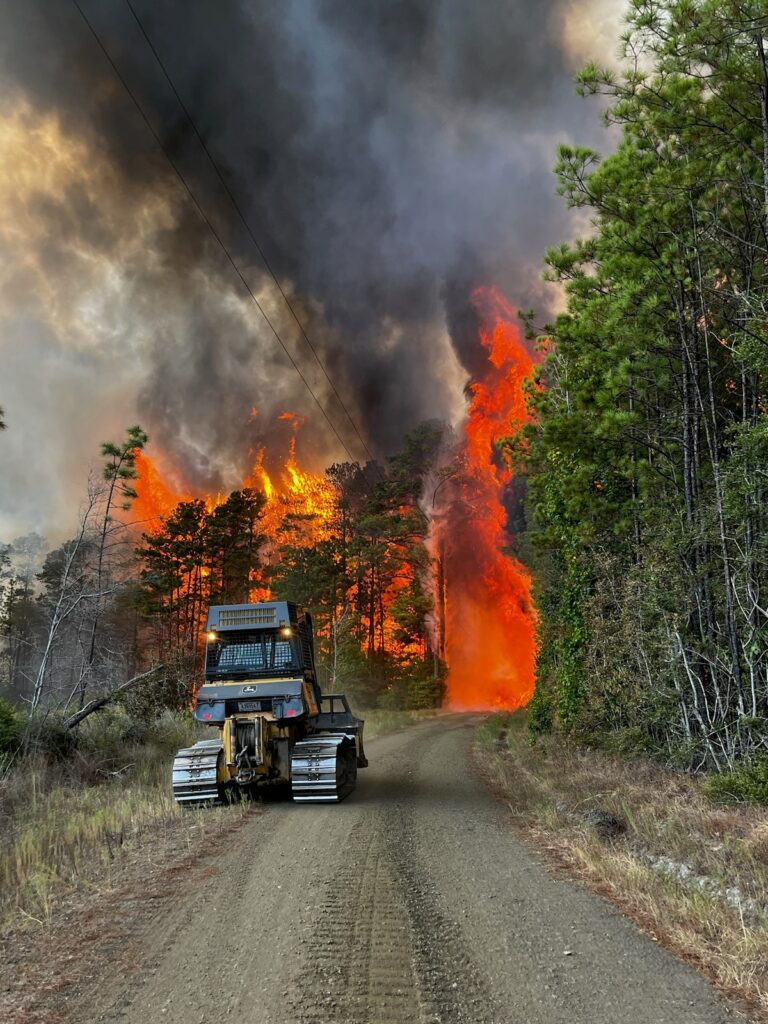 bulldozer driving toward a wildfire in the background