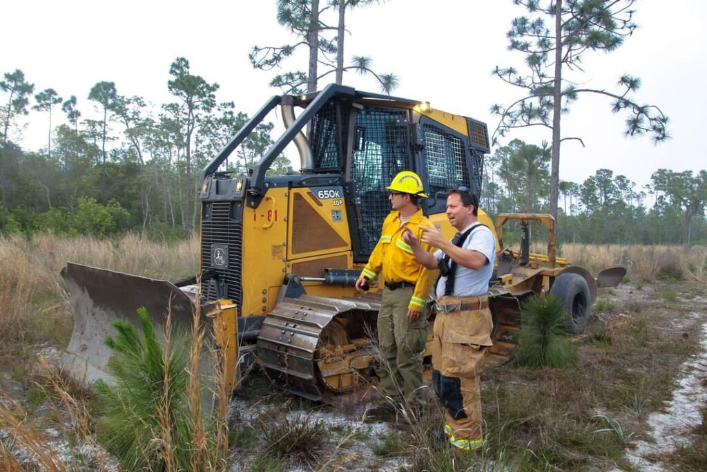 wildland firefighter in PPE speaking to a structure firefighter next to a firefighting bulldozer