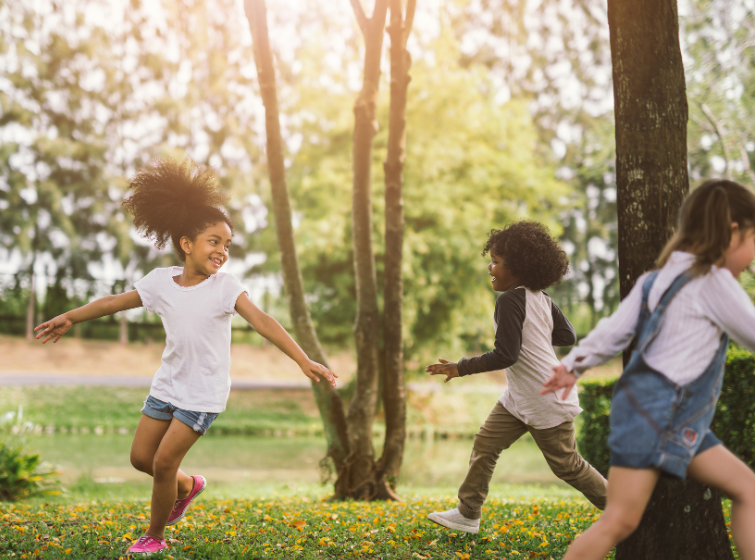 Group of children playing and running in a natural area of a local park.