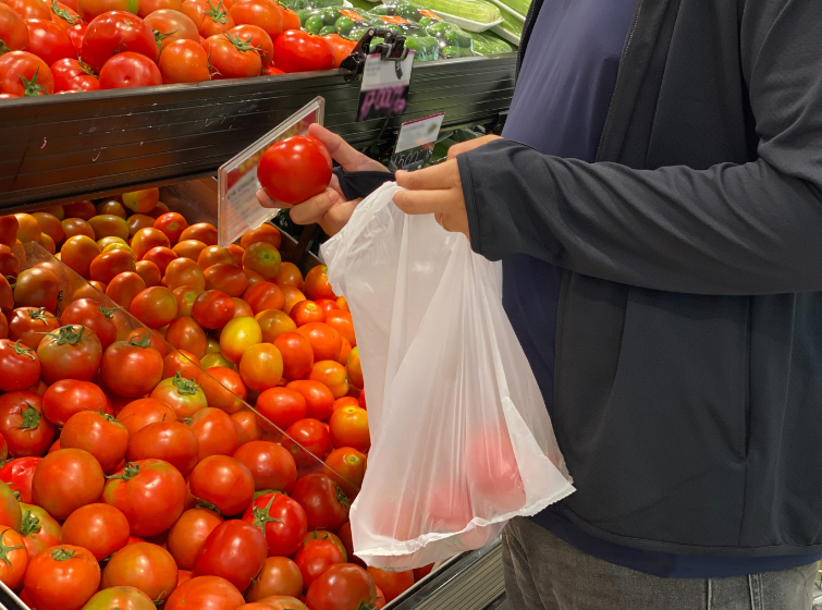 Man at a grocery store putting a tomato in a plastic bag made from trees