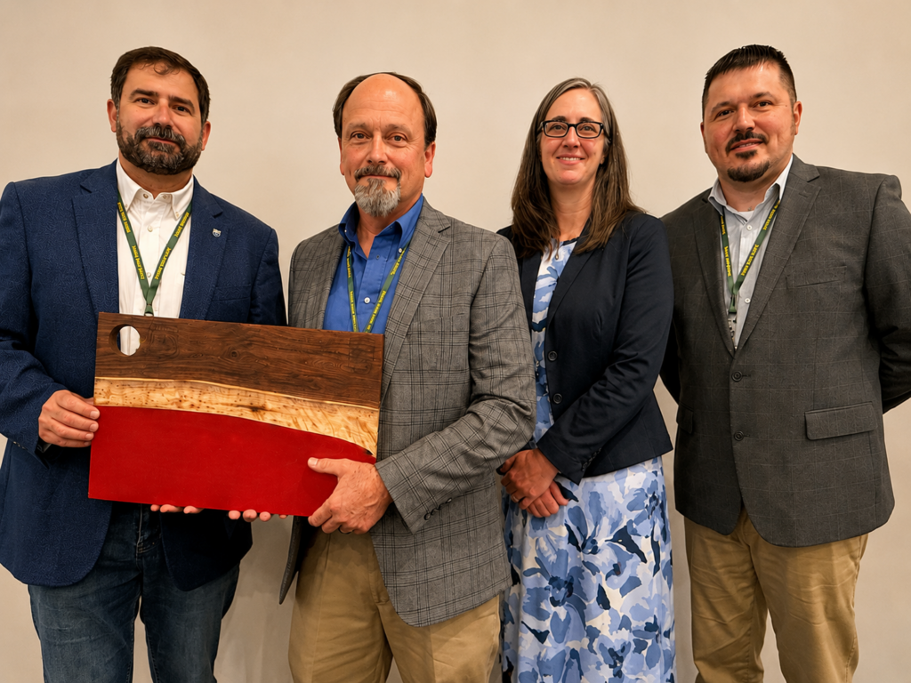 Four forestry professionals stand together against a light-colored wall at an awards ceremony. The group includes three men and one woman wearing conference lanyards and business attire. Two of the individuals hold a large handcrafted wooden award featuring natural wood grain and a bold red accent. All four are smiling and facing the camera.